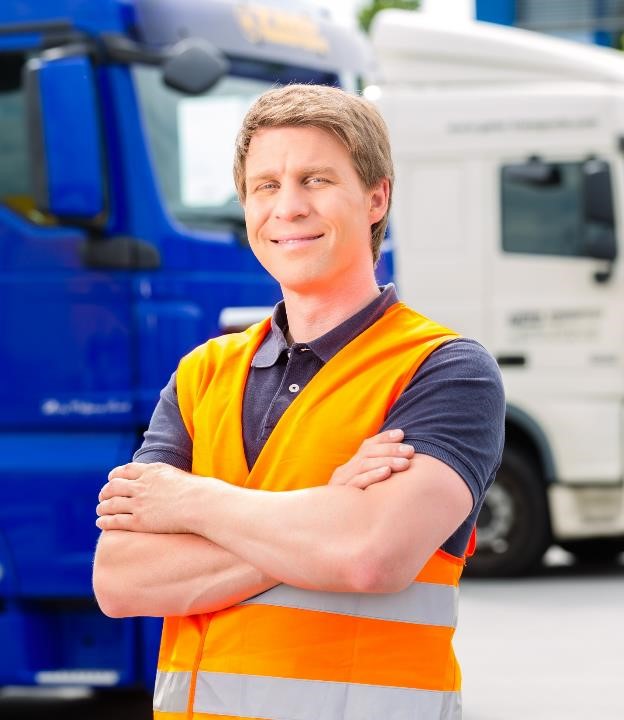 A man wearing a high vis vest stood in front of some lorries.