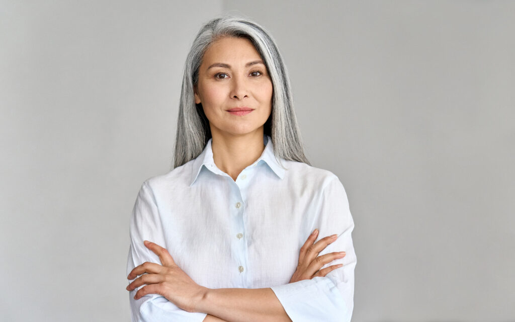 Middle aged smart woman stood with her arms folded in front of a plain background.