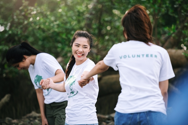 3 volunteers holding hands and smiling, all wearing white volunteer t-shirts.