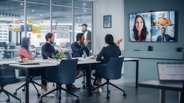 A group of 4 employees in a conference room on a video call to 3 other individuals.